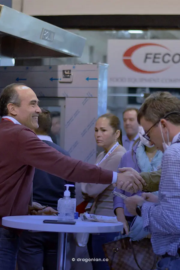 Hombre sonriendo y estrechando la mano de un hombre adulto en una feria de alimentos Alimentarte.